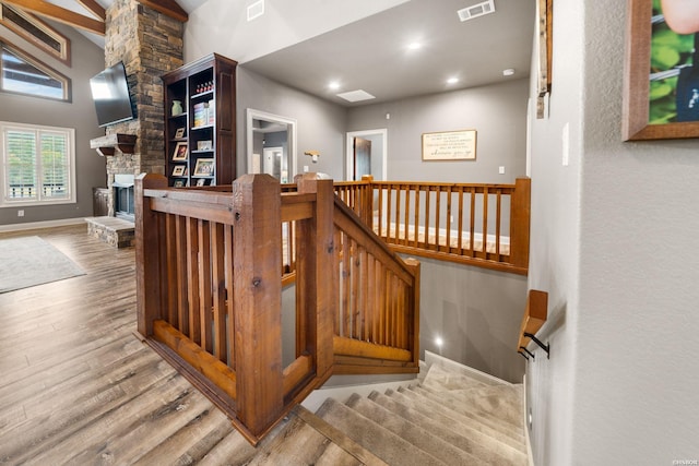 staircase featuring high vaulted ceiling, a fireplace, wood finished floors, visible vents, and baseboards