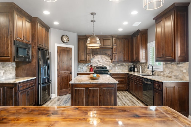 kitchen featuring light wood-style floors, a sink, light stone counters, and black appliances