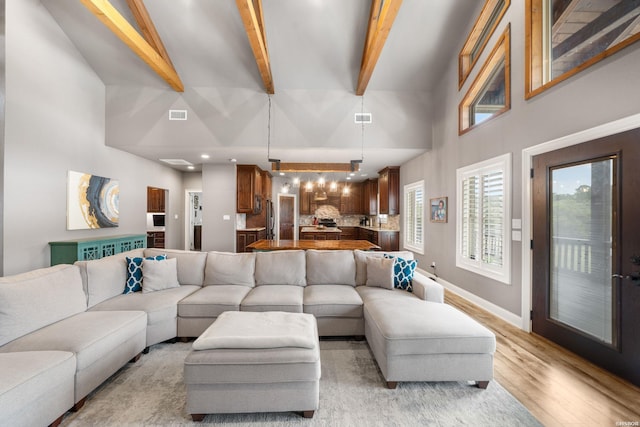 living area featuring visible vents, light wood finished floors, beamed ceiling, and a high ceiling