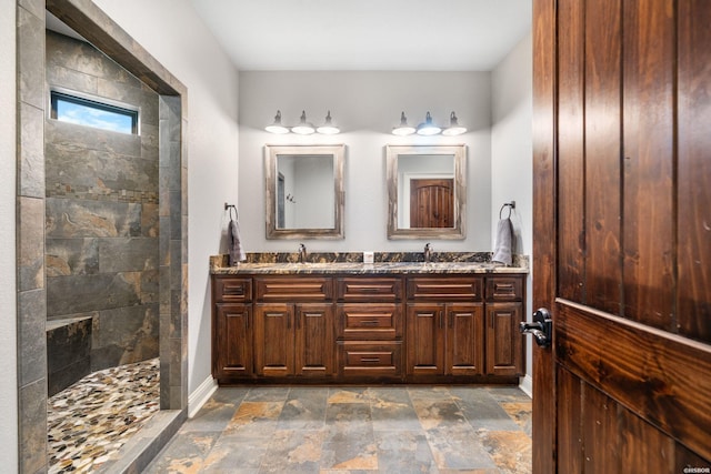 bathroom with double vanity, stone finish flooring, a walk in shower, and a sink