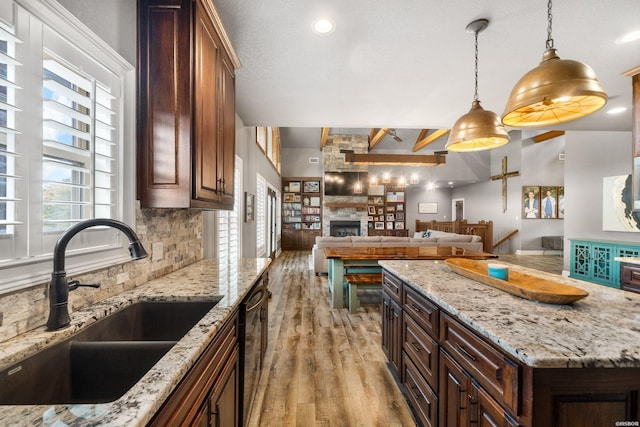 kitchen featuring light wood finished floors, tasteful backsplash, open floor plan, a fireplace, and a sink