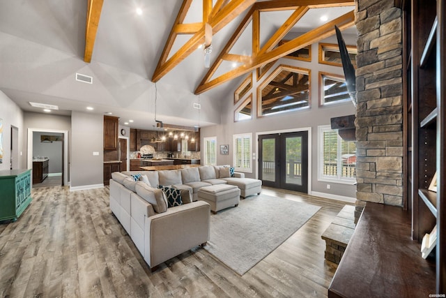 living area with baseboards, visible vents, wood finished floors, french doors, and high vaulted ceiling