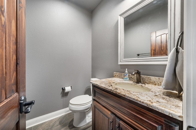 bathroom featuring toilet, a textured wall, baseboards, and vanity