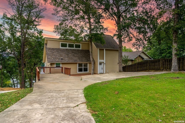 view of front facade featuring driveway, a shingled roof, fence, and a front yard