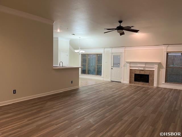 unfurnished living room featuring dark wood-type flooring, a fireplace, baseboards, and ceiling fan with notable chandelier