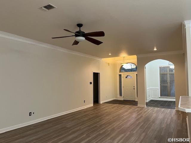 spare room featuring arched walkways, dark wood-style flooring, visible vents, ornamental molding, and baseboards