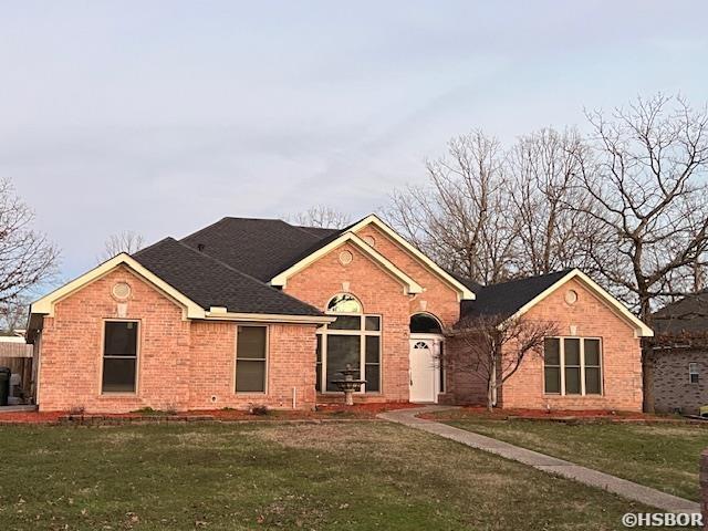 ranch-style house featuring brick siding, roof with shingles, and a front yard