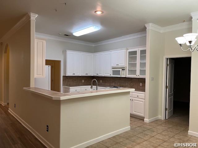 kitchen featuring arched walkways, white appliances, white cabinets, decorative backsplash, and crown molding