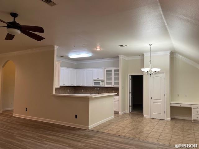 kitchen featuring arched walkways, visible vents, decorative backsplash, white microwave, and ornamental molding