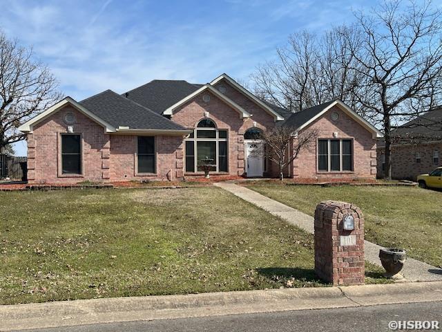 ranch-style house with brick siding, a front yard, and a shingled roof