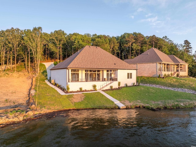 rear view of property with stucco siding, a yard, and a water view