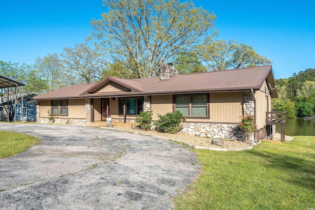 ranch-style home featuring aphalt driveway, a chimney, metal roof, stone siding, and a front lawn