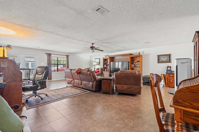 living room featuring light tile patterned floors, visible vents, a textured ceiling, and ceiling fan