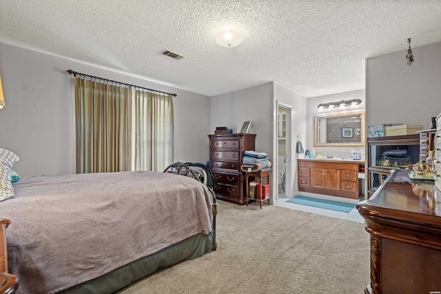 bedroom featuring carpet, visible vents, ensuite bathroom, and a textured ceiling