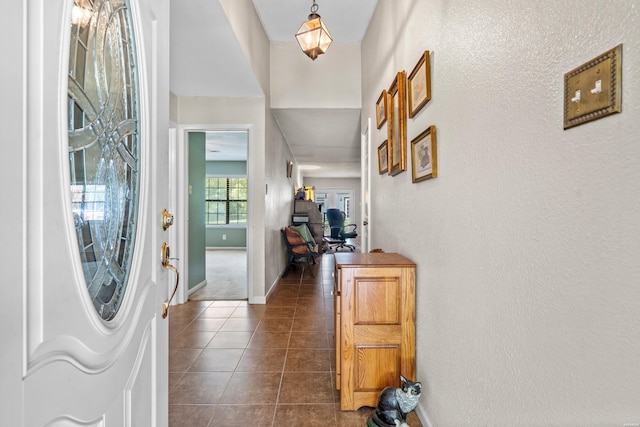 foyer with baseboards, dark tile patterned floors, and a textured wall