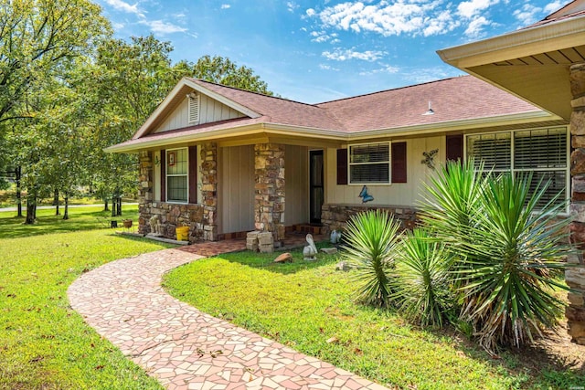 view of front of property featuring a front yard, stone siding, and roof with shingles