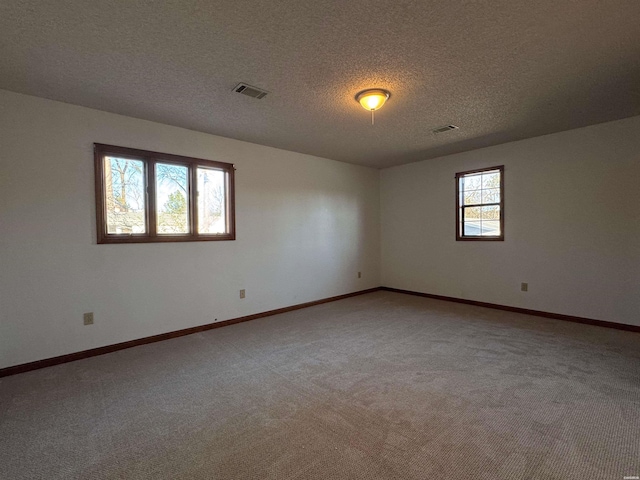 spare room featuring baseboards, a textured ceiling, visible vents, and light colored carpet