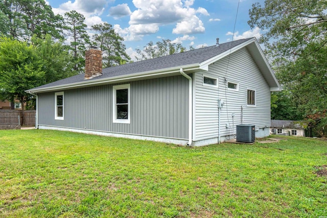 view of home's exterior featuring roof with shingles, a chimney, central air condition unit, a lawn, and fence