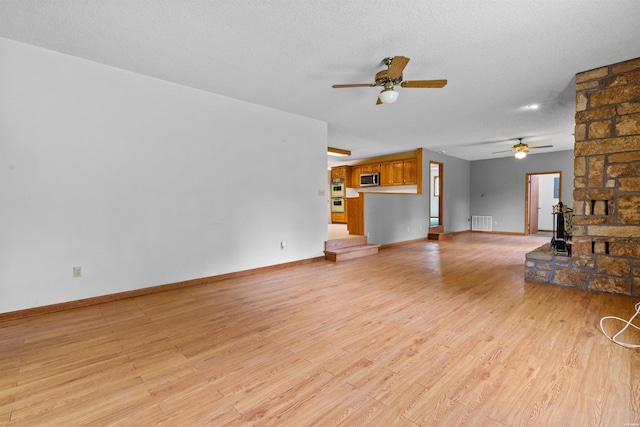 unfurnished living room featuring light wood-style floors, a textured ceiling, and baseboards