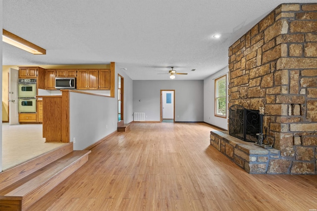 unfurnished living room featuring a textured ceiling, ceiling fan, light wood-style flooring, a fireplace, and visible vents