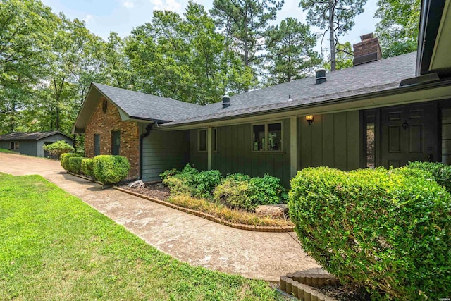 view of side of property with brick siding, a yard, roof with shingles, board and batten siding, and a chimney