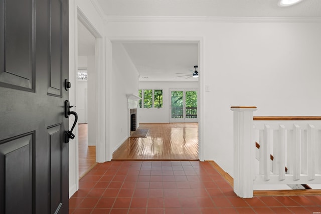 foyer with a ceiling fan, dark tile patterned flooring, a brick fireplace, and crown molding