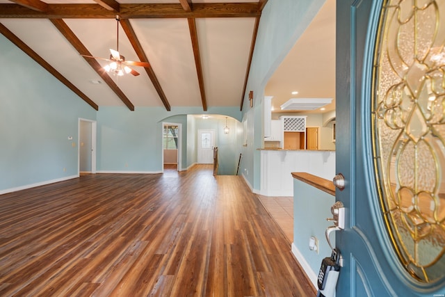 unfurnished living room with baseboards, arched walkways, ceiling fan, beamed ceiling, and wood finished floors