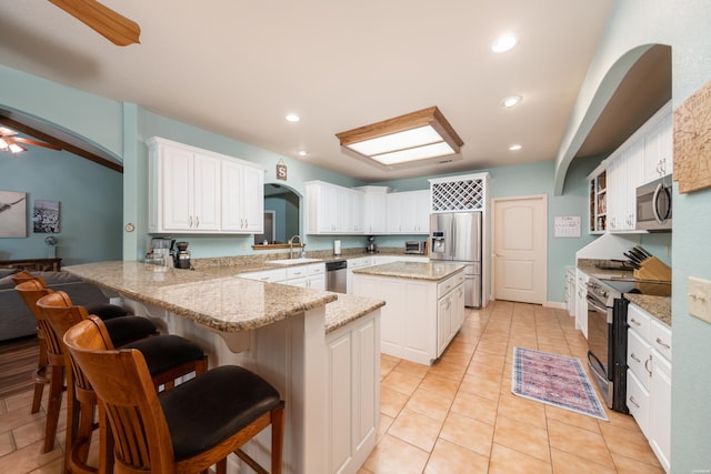 kitchen featuring a peninsula, a kitchen breakfast bar, white cabinets, appliances with stainless steel finishes, and a center island