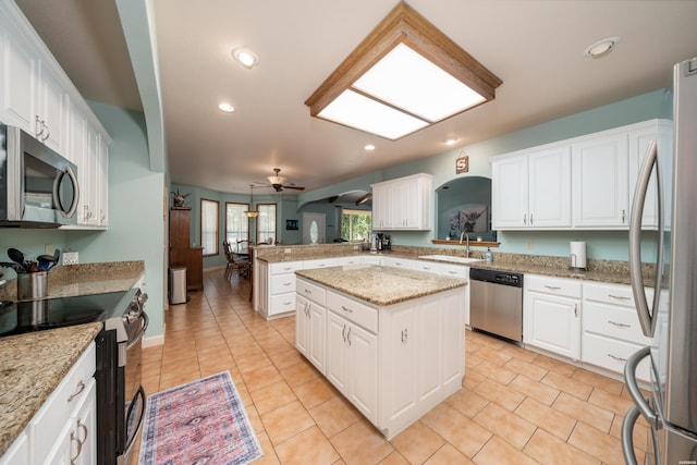 kitchen with stainless steel appliances, a peninsula, a sink, a kitchen island, and white cabinetry