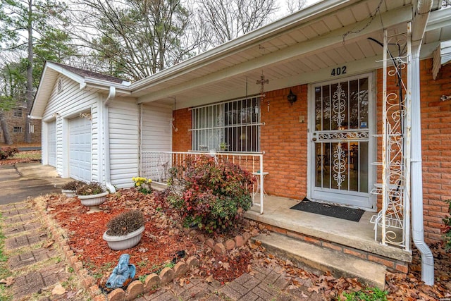 entrance to property with an attached garage, covered porch, and brick siding