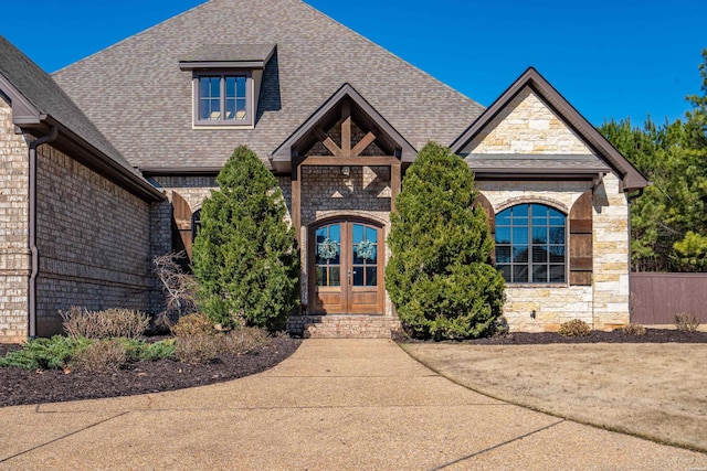 view of front facade with a shingled roof, french doors, and stone siding