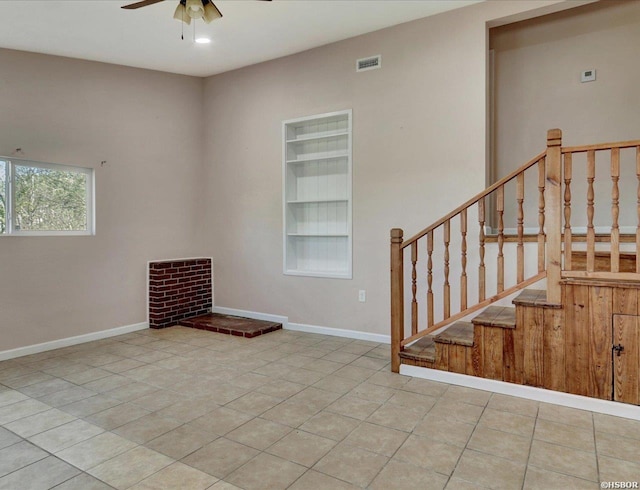 tiled empty room featuring visible vents, ceiling fan, built in shelves, and baseboards