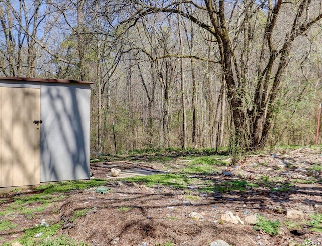 view of yard featuring a storage unit, an outbuilding, and a wooded view