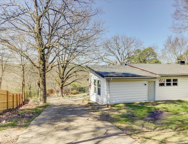 view of side of home with fence, driveway, and a shingled roof