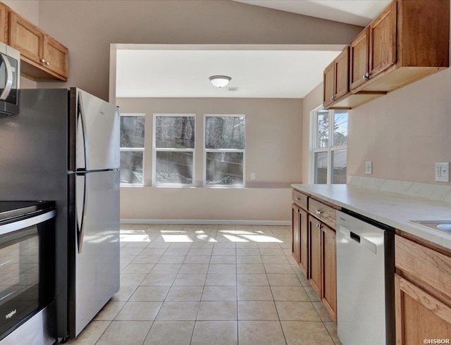 kitchen featuring baseboards, light countertops, brown cabinets, light tile patterned flooring, and stainless steel appliances