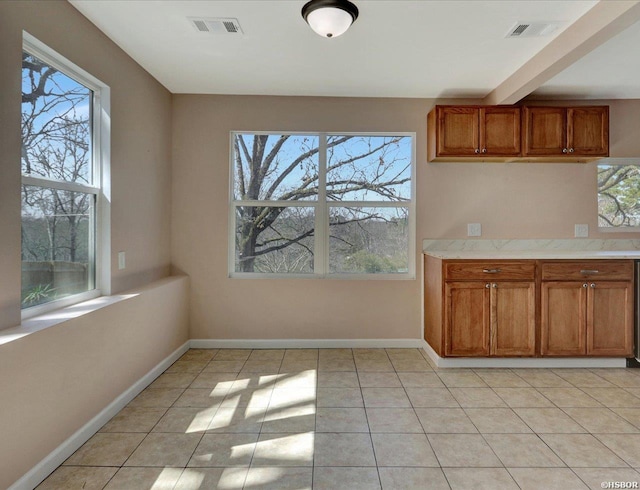 unfurnished dining area featuring light tile patterned floors, visible vents, baseboards, and a healthy amount of sunlight