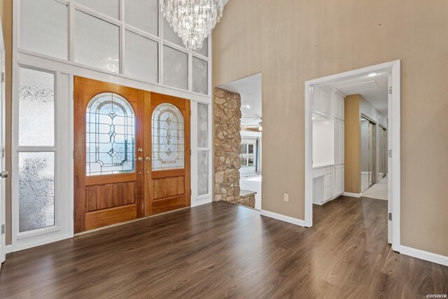 foyer entrance with dark wood-style floors, french doors, a towering ceiling, an inviting chandelier, and baseboards