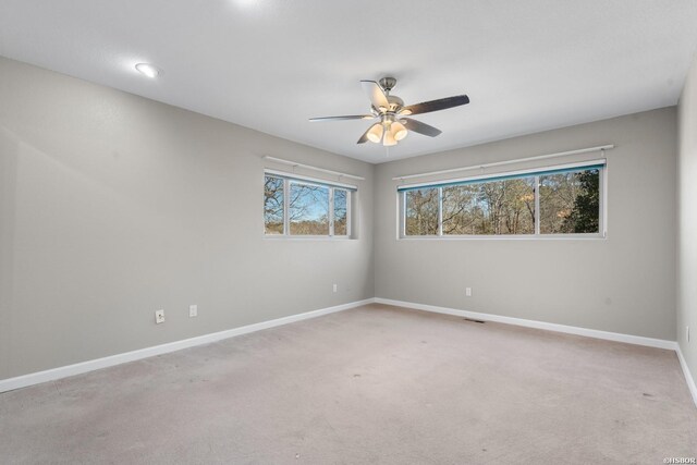 empty room featuring a ceiling fan, light colored carpet, and baseboards