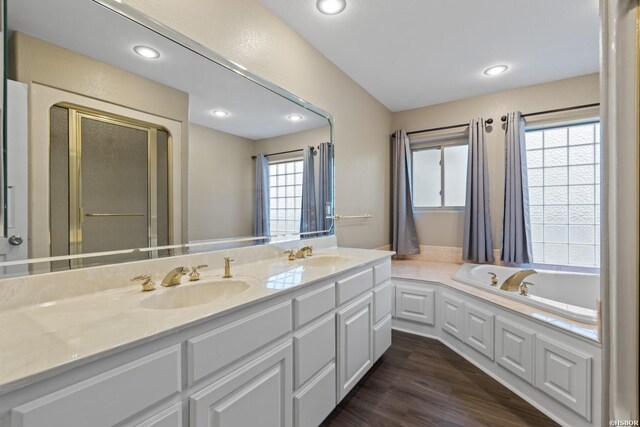 bathroom featuring double vanity, a bath, a sink, and wood finished floors