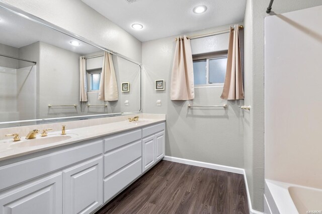 bathroom with double vanity, wood finished floors, a sink, and baseboards