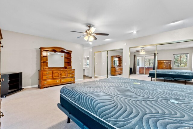 bedroom featuring a ceiling fan, light carpet, baseboards, and two closets