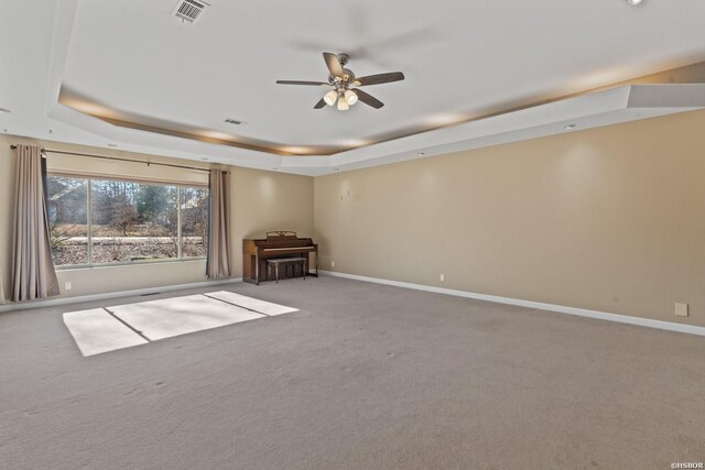 spare room with ceiling fan, light colored carpet, visible vents, baseboards, and a tray ceiling