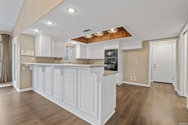 kitchen with a peninsula, visible vents, white cabinetry, light countertops, and black appliances