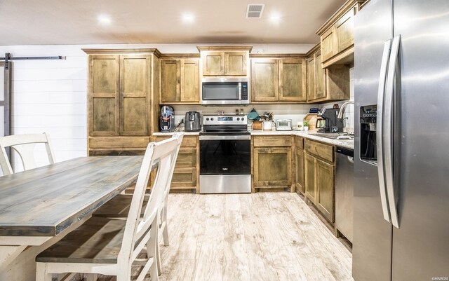 kitchen with a barn door, visible vents, light wood-style flooring, stainless steel appliances, and a sink