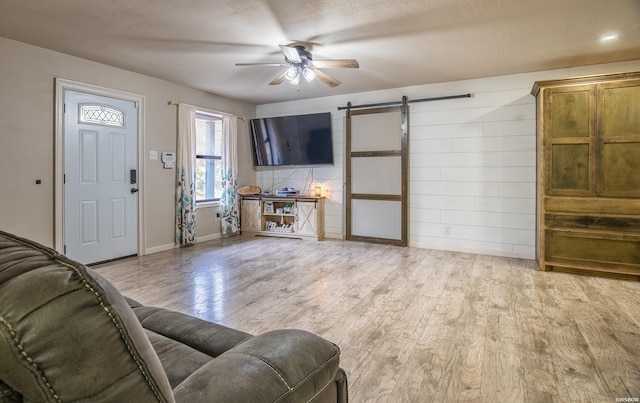 living room featuring light wood finished floors, a barn door, ceiling fan, and a textured ceiling