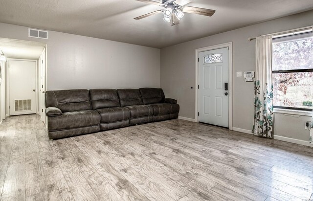 living room with visible vents, ceiling fan, light wood-style flooring, and baseboards