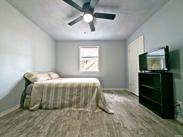 bedroom with ceiling fan, a textured ceiling, baseboards, and wood finished floors