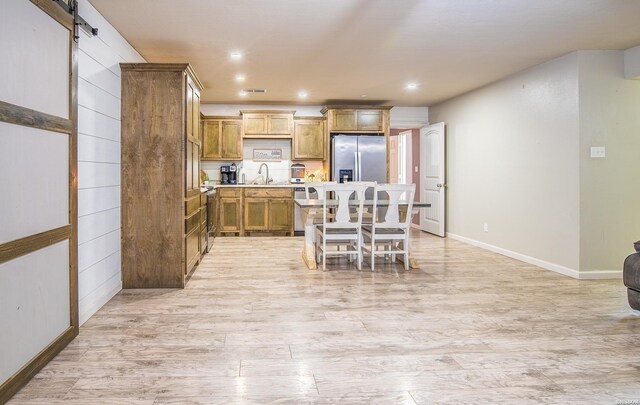 kitchen featuring brown cabinets, stainless steel refrigerator with ice dispenser, light countertops, light wood-style floors, and a sink