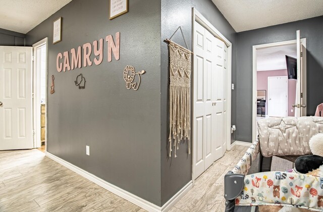 hall featuring a textured ceiling, wood finished floors, and baseboards