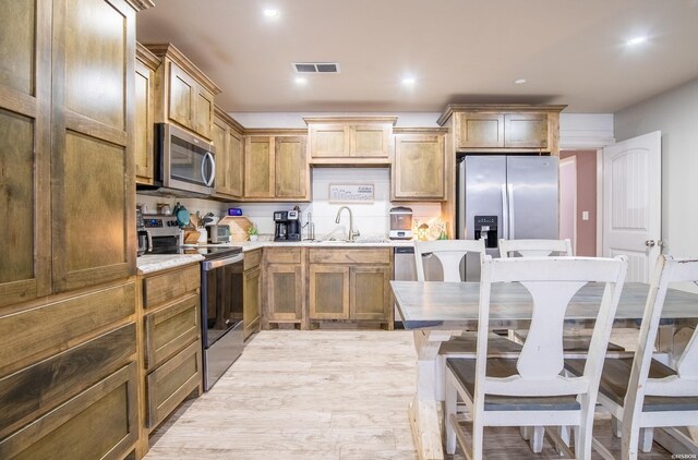 kitchen featuring a breakfast bar, visible vents, appliances with stainless steel finishes, brown cabinetry, and a sink